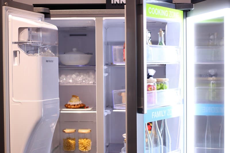 Technician clearing defrost drain tube and checking drain pan in refrigerator